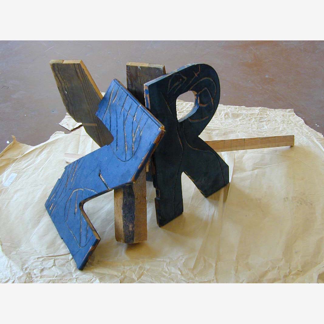 Three wooden letter types covered with black paint standing on the floor 
and leaning against each other, V, R, Z.